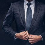 Cropped portrait of a successful businessman buttoning his elegant suit. Isolated on a dark background.